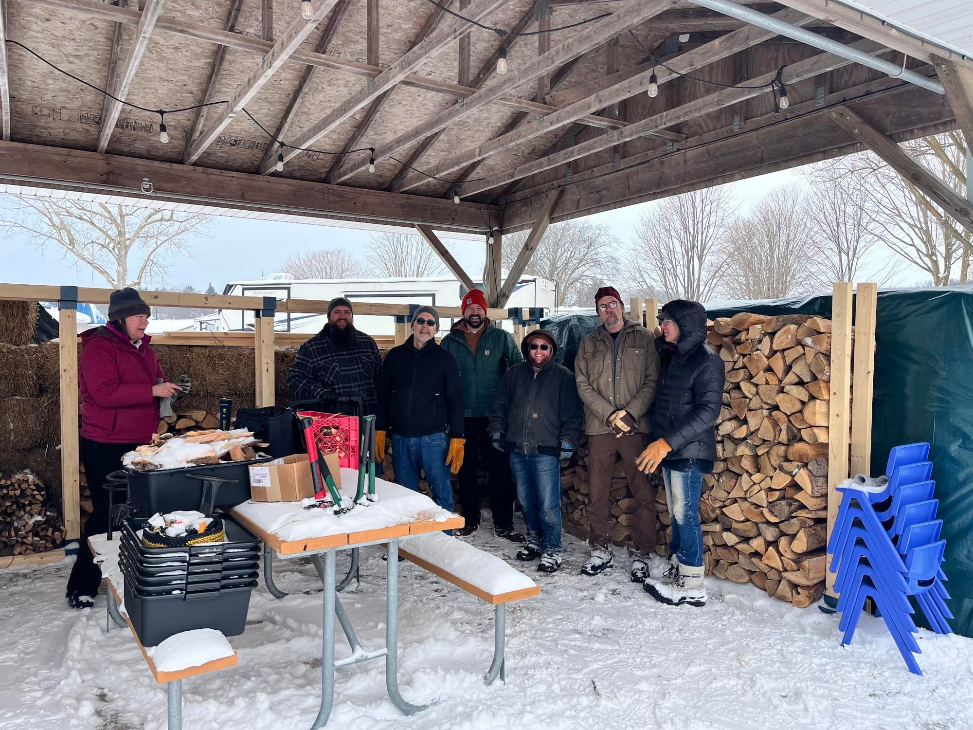 A group of local Commoners standing next to a big stack of firewood they moved. They are bundled up warm because it was about 28 degrees Fahrenheit.