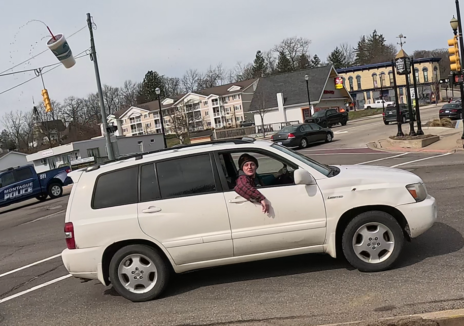 A white kid in a red plaid shirt is throwing a full cup of soda out the window of a white Toyota SUV. In the background, we see Montague Police truck, and the corner of Dowling and Water Streets in Montague.