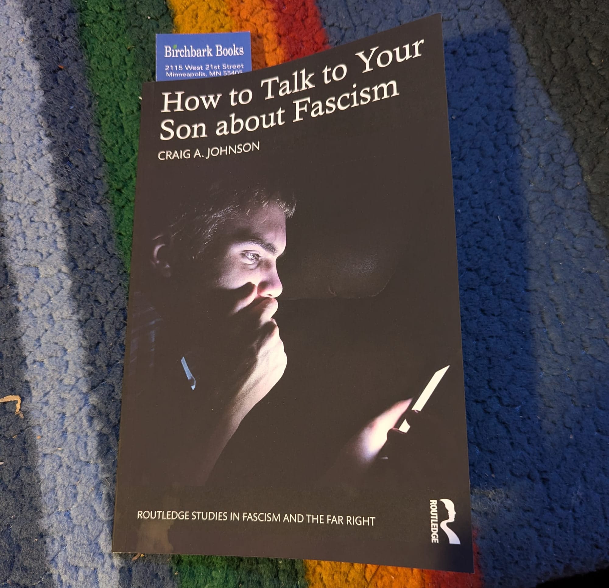 A copy of "How to Talk to Your Son about Fascism" by Craig A Johnson. The cover shows a young white man in a dark room reading something on his screen.