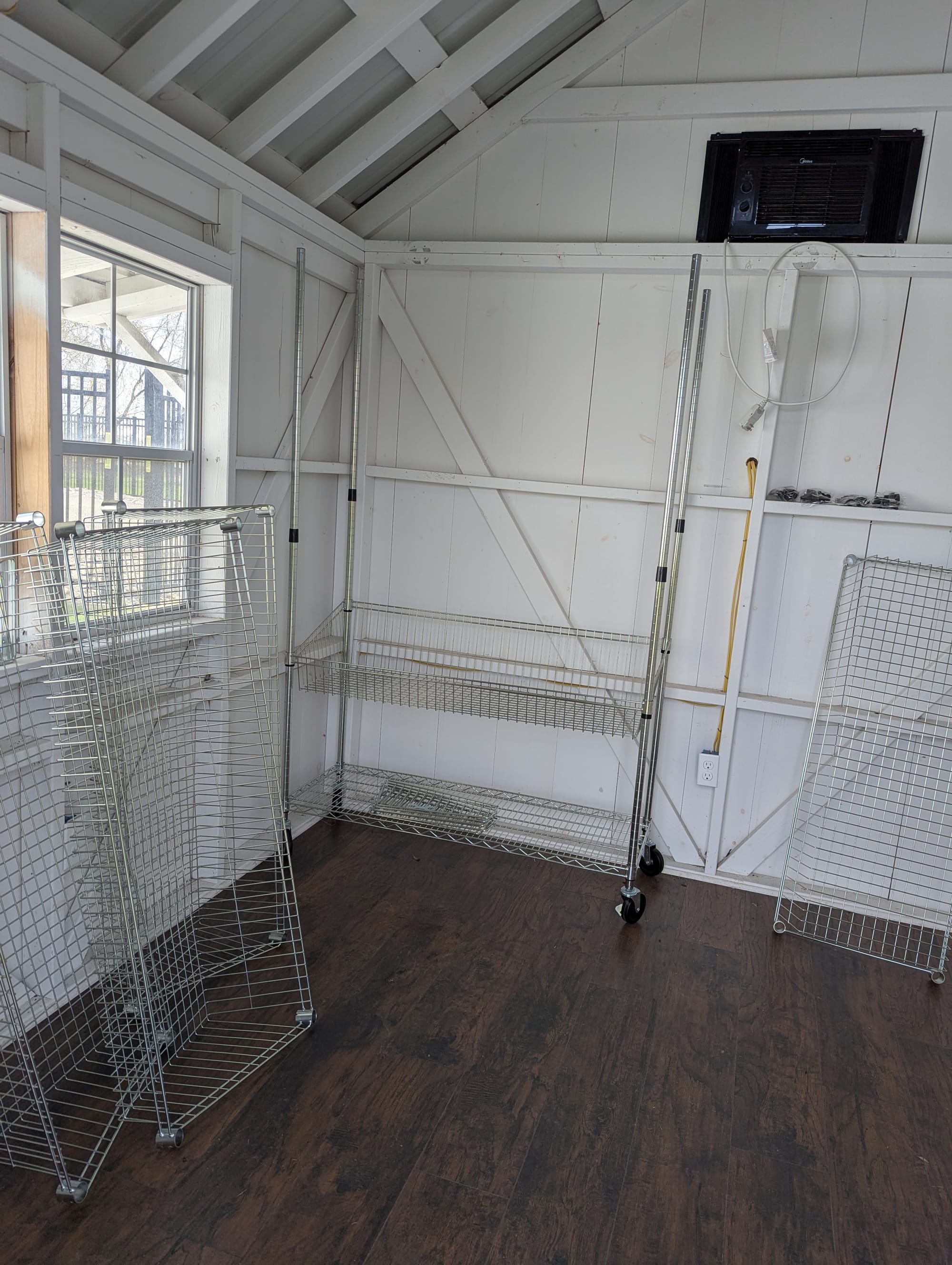 The inside of a white shed with a dark paneled floor. Along the wall is one of those sets of adjustable wire shelves that are designed for use in commercial kitchens but are beloved by Costco members everywhere