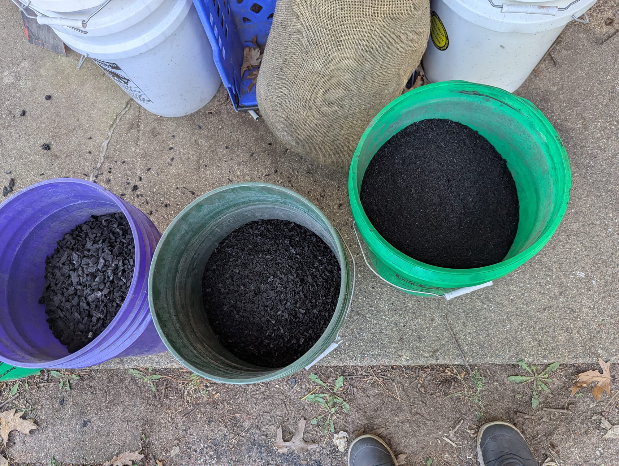 Three five gallon buckets, each with a different size of biochar inside