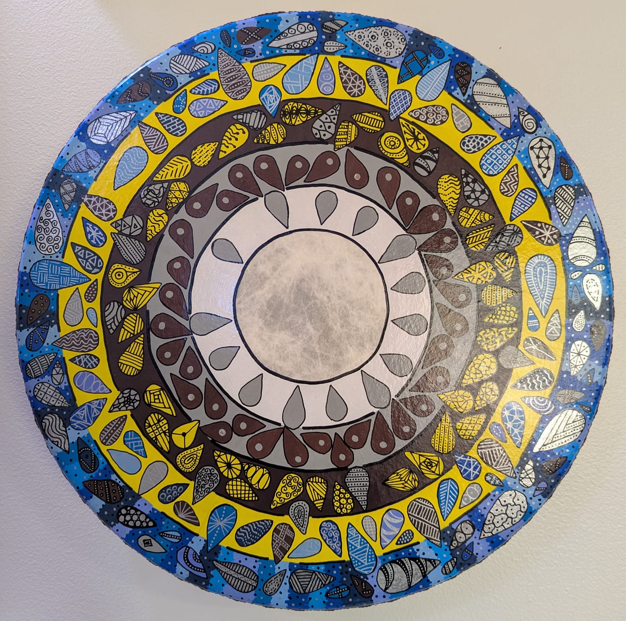 An intricately-painted hand drum showing concentric rings with little teardrop-shaped "inhabitants"
