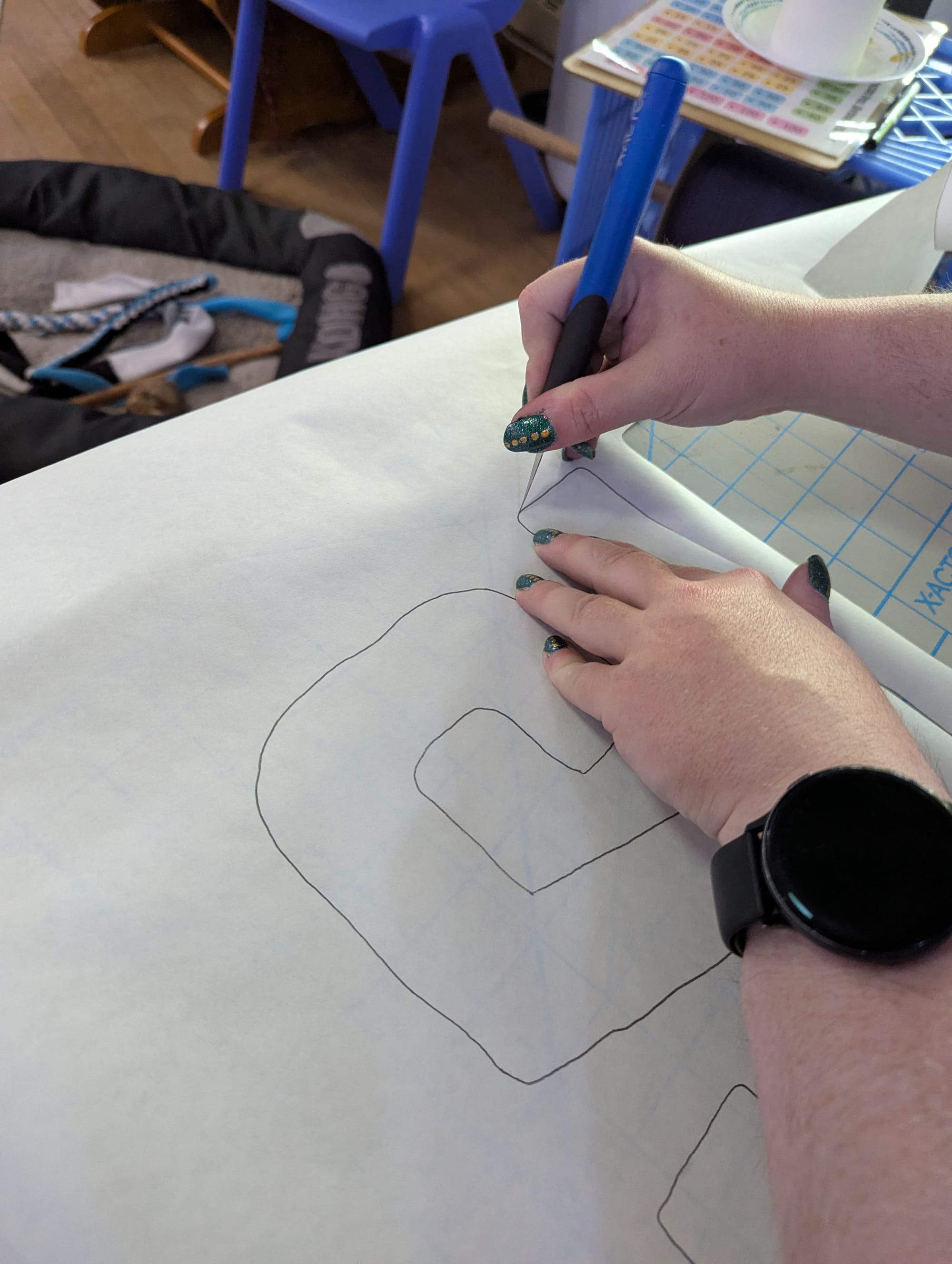 A pair of hands holding the freezer paper from the previous image and cutting out the letters with an exacto knife