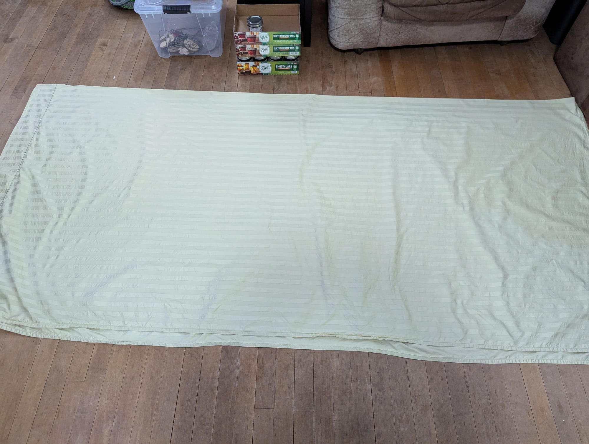 A large satin-striped sheet folded in half and laying on a rough wooden floor