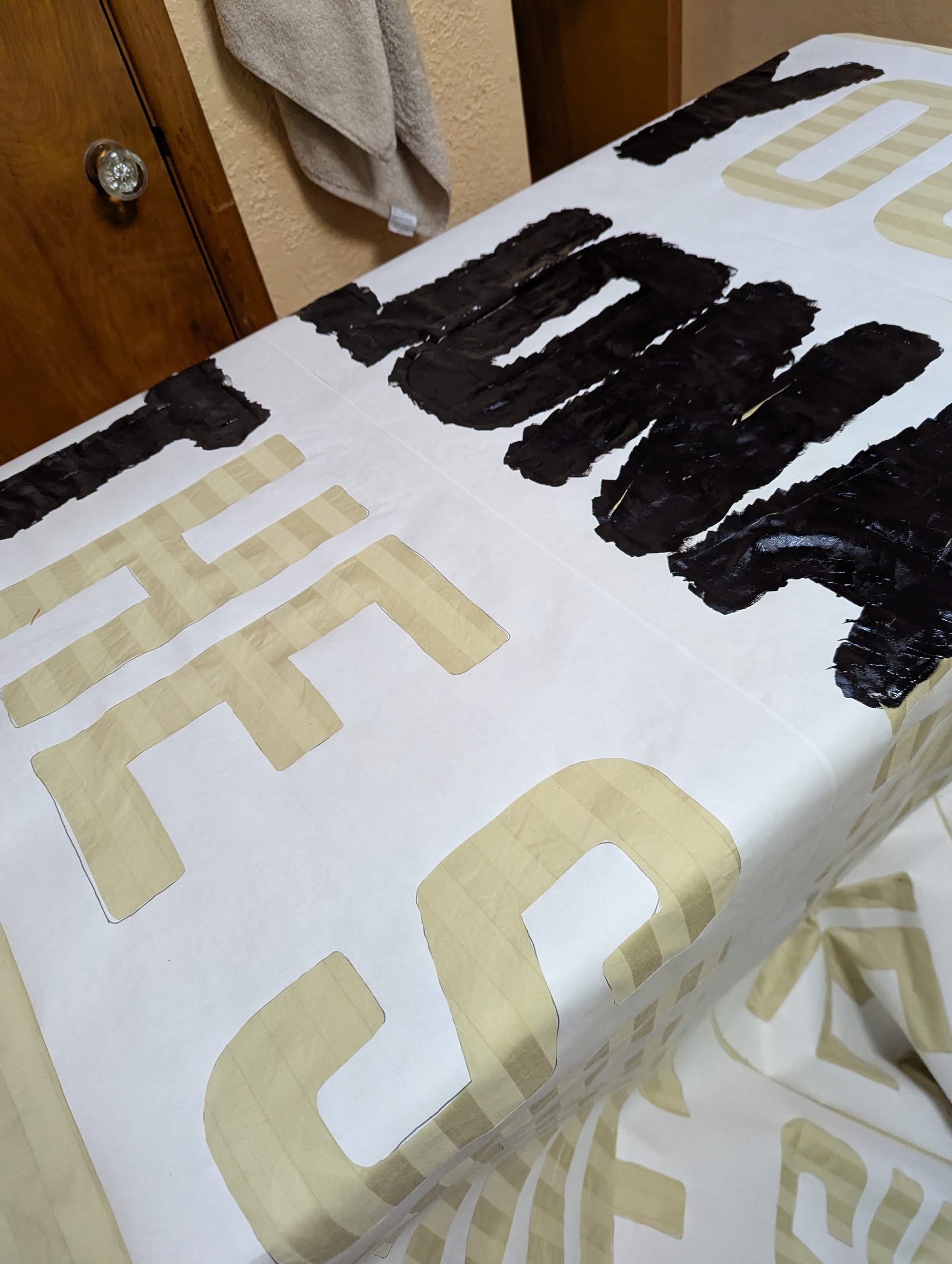 The banner in the middle of being painted. Some of the stencil letters have been painted in, and some are still blank.