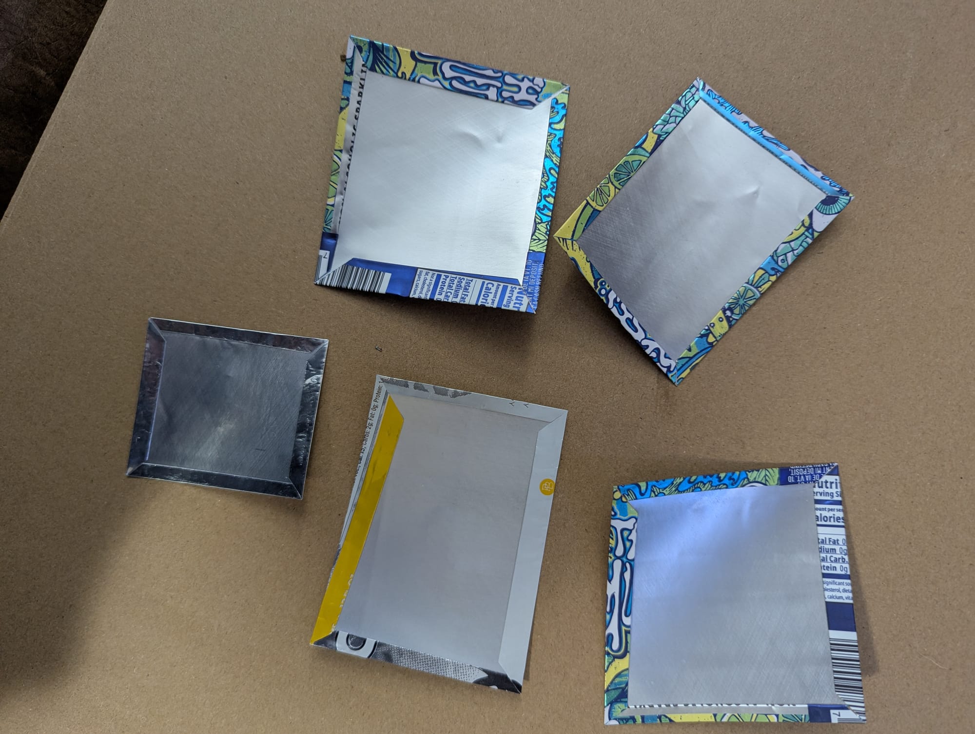 Five plant tags made from recycled aluminum. There is a narrow border along each edge where the metal has been folded over and the pattern of the original tag shows through