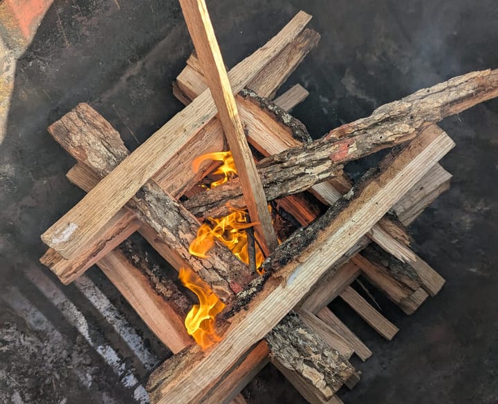 A small log-cabin-style campfire in the early stages of ignition