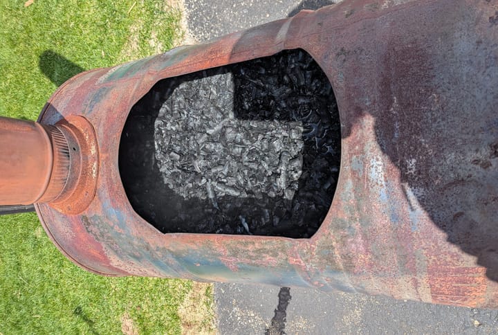A slightly rusty 55-gallon steel barrel that has been converted into a stove. The top is open, showing that it is full of biochar.