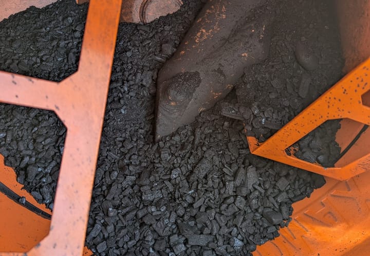 The inside of an orange cement mixer. It is about one-third full of smooth, river-rock-like pieces of biochar in various sizes.