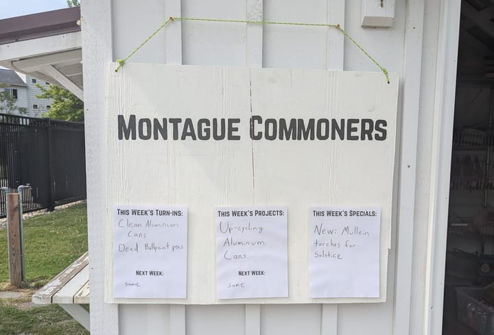 The new sign for the Montague Commoners shed at the Artisan market. It is a large plywood board painted white, with "Montague Commoners" in black lettering at the top.