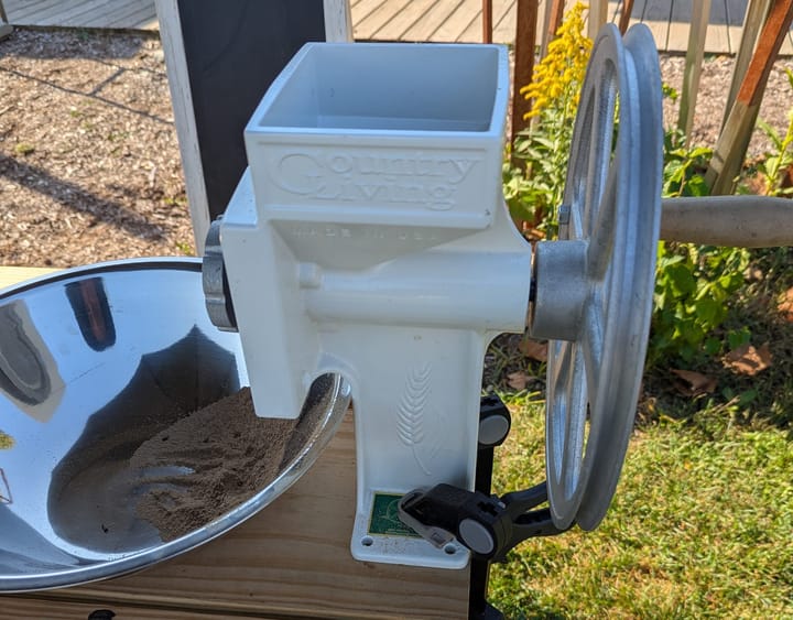 A white Country Living hand-crank flour mill attached to the end of a picnic table at the Artisan Market